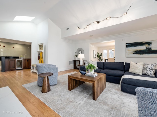 living room with a skylight, high vaulted ceiling, light hardwood / wood-style flooring, ornamental molding, and beverage cooler