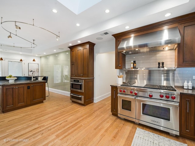 kitchen featuring sink, stainless steel appliances, light hardwood / wood-style floors, decorative backsplash, and wall chimney exhaust hood