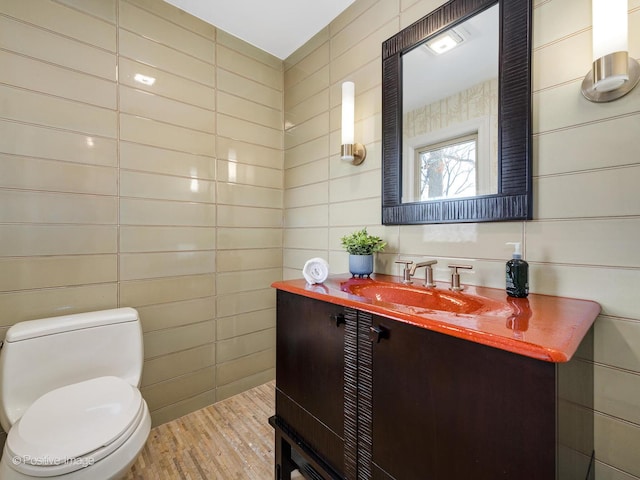 bathroom with wood-type flooring, toilet, vanity, and tile walls