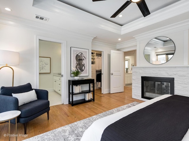 bedroom featuring crown molding, light hardwood / wood-style flooring, connected bathroom, a tray ceiling, and a fireplace