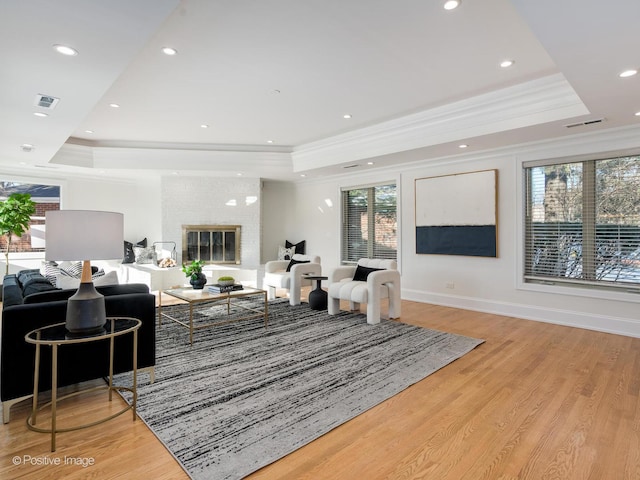 living room featuring crown molding, a brick fireplace, a raised ceiling, and light hardwood / wood-style flooring