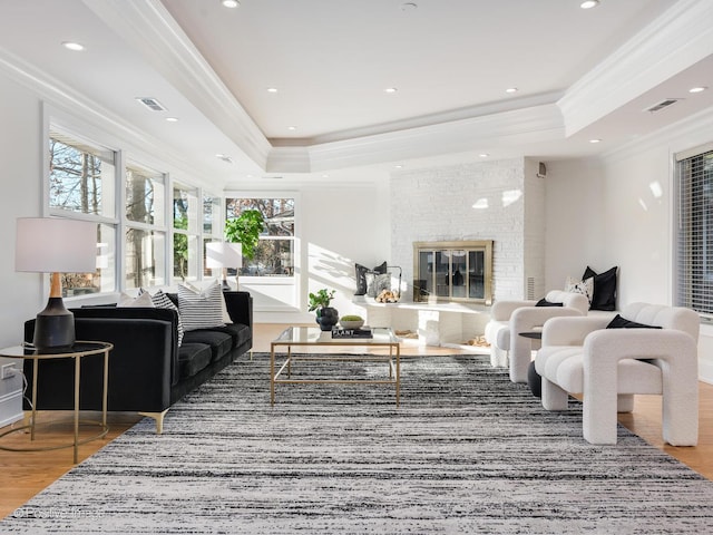 living room with ornamental molding, wood-type flooring, a large fireplace, and a tray ceiling