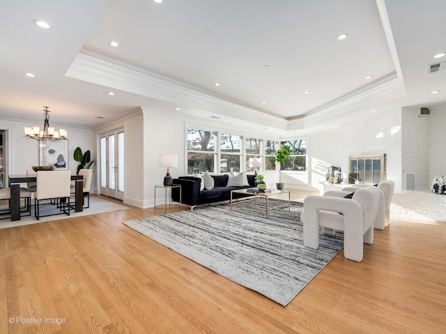 living room featuring an inviting chandelier, crown molding, light hardwood / wood-style floors, and a raised ceiling