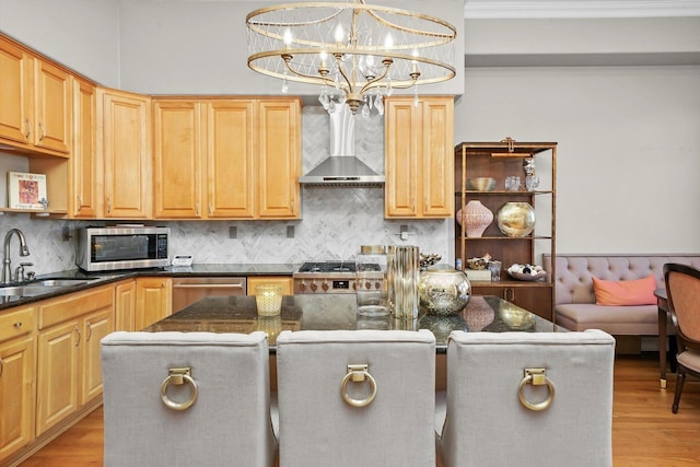 kitchen with appliances with stainless steel finishes, a center island, sink, wall chimney range hood, and decorative light fixtures