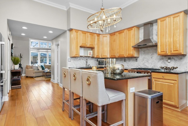 kitchen featuring appliances with stainless steel finishes, hanging light fixtures, light brown cabinetry, a kitchen island, and wall chimney exhaust hood