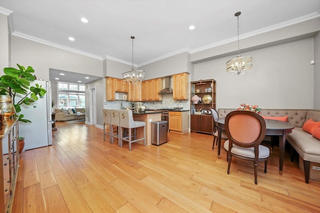 kitchen featuring fridge, a kitchen bar, light hardwood / wood-style floors, wall chimney range hood, and pendant lighting