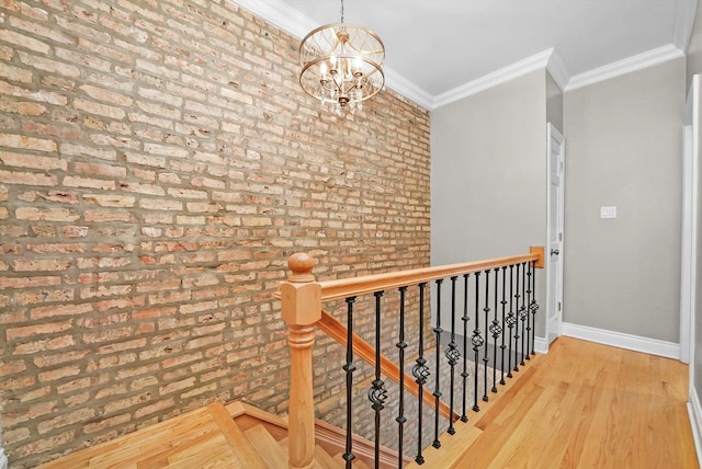 hallway with brick wall, an inviting chandelier, crown molding, and light hardwood / wood-style flooring