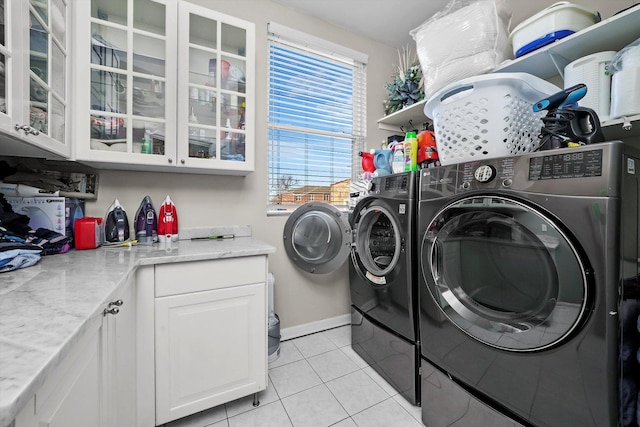 clothes washing area with washer and dryer, cabinets, and light tile patterned floors