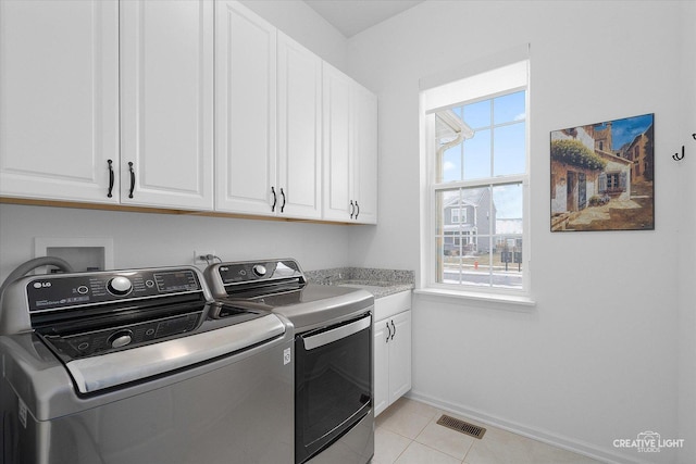 laundry room with washing machine and dryer, cabinets, and light tile patterned flooring