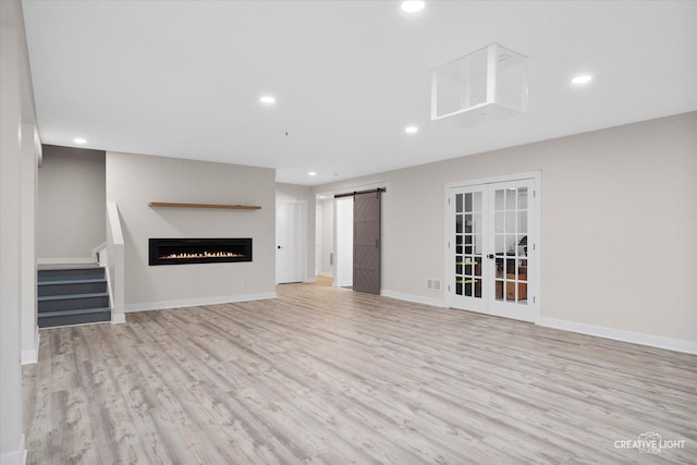 unfurnished living room with french doors, a barn door, and light wood-type flooring