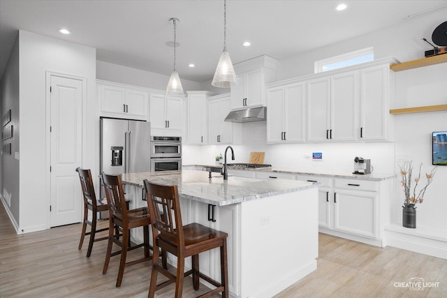 kitchen with a kitchen bar, white cabinetry, stainless steel appliances, hanging light fixtures, and a center island with sink