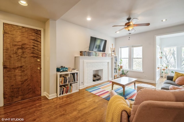 living room with hardwood / wood-style flooring, ceiling fan, and a brick fireplace