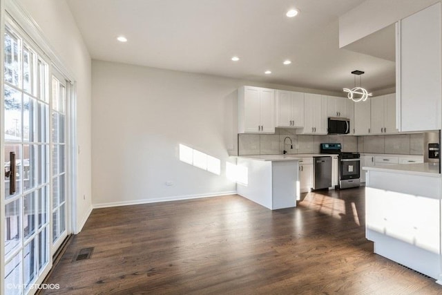 kitchen with pendant lighting, dark hardwood / wood-style floors, backsplash, white cabinetry, and appliances with stainless steel finishes