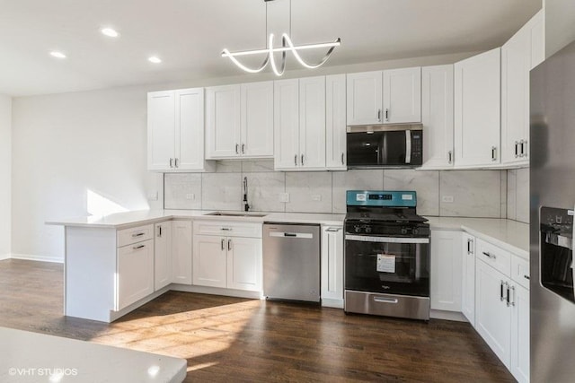 kitchen featuring appliances with stainless steel finishes, hanging light fixtures, kitchen peninsula, white cabinets, and sink