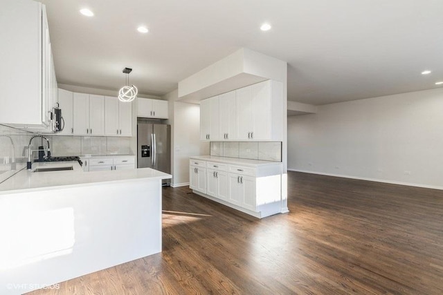 kitchen with stainless steel fridge with ice dispenser, hanging light fixtures, sink, white cabinetry, and backsplash