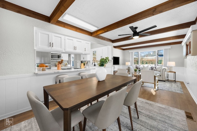 dining space with light wood-type flooring, ceiling fan, a textured ceiling, and beamed ceiling