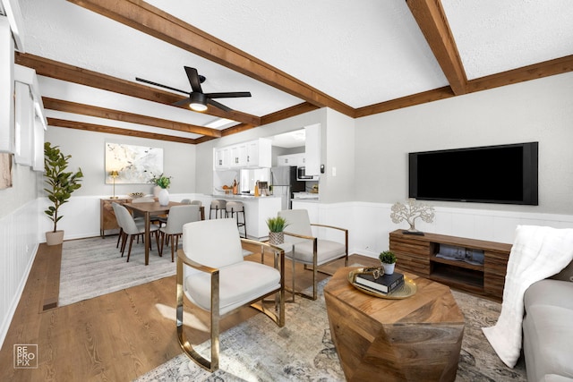 living room with a textured ceiling, beam ceiling, ceiling fan, and light hardwood / wood-style floors