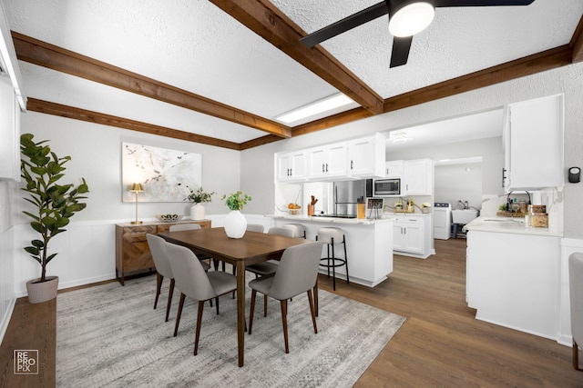 dining space with a textured ceiling, dark wood-type flooring, beamed ceiling, and ceiling fan