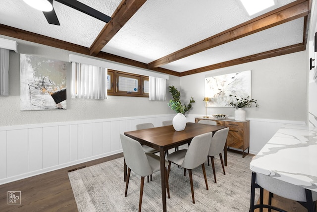 dining space with a textured ceiling, wood-type flooring, ceiling fan, and beamed ceiling