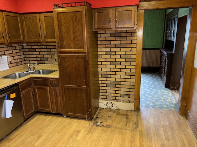 kitchen featuring sink, light hardwood / wood-style flooring, dishwasher, and brick wall