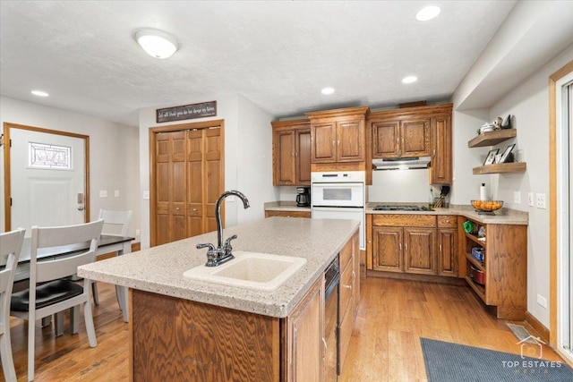 kitchen with double oven, sink, a kitchen island with sink, black gas stovetop, and light hardwood / wood-style flooring