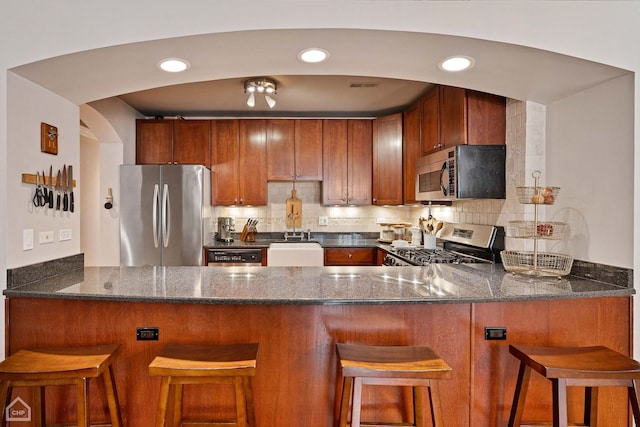 kitchen with kitchen peninsula, appliances with stainless steel finishes, decorative backsplash, and a kitchen bar