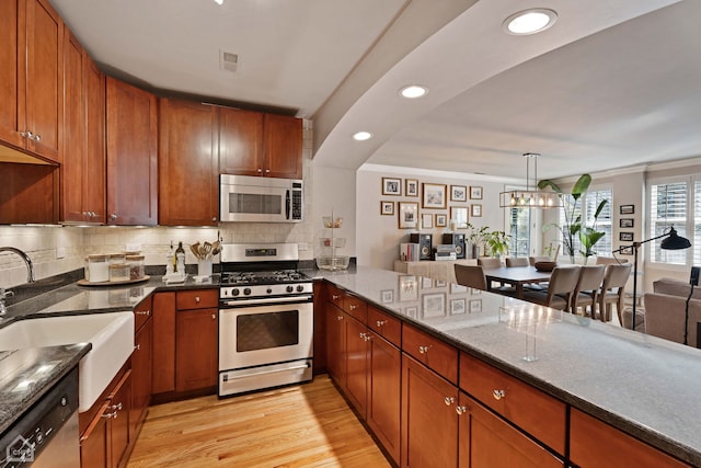 kitchen featuring decorative light fixtures, an inviting chandelier, light hardwood / wood-style floors, dark stone counters, and appliances with stainless steel finishes