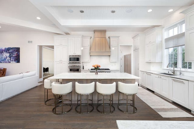 kitchen with custom exhaust hood, a kitchen island with sink, sink, and stainless steel appliances