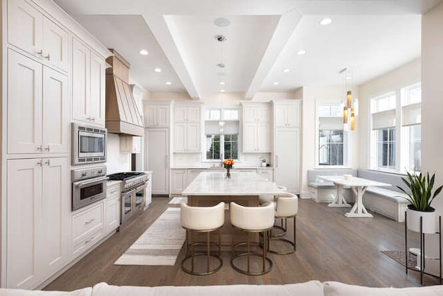 kitchen featuring appliances with stainless steel finishes, a center island, a kitchen bar, decorative light fixtures, and custom exhaust hood