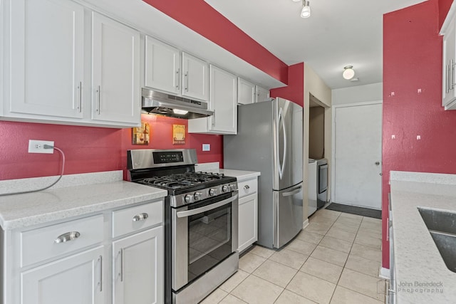 kitchen featuring independent washer and dryer, white cabinetry, stainless steel appliances, light stone counters, and light tile patterned flooring