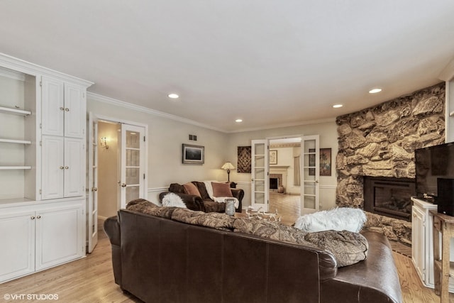 living room featuring ornamental molding, a stone fireplace, and light hardwood / wood-style floors