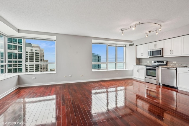 kitchen with stainless steel appliances, white cabinetry, dark wood-type flooring, and light stone countertops