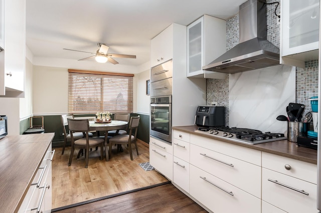 kitchen with appliances with stainless steel finishes, decorative backsplash, dark hardwood / wood-style floors, wall chimney range hood, and white cabinets