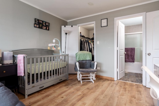 bedroom with a walk in closet, a crib, ornamental molding, and light hardwood / wood-style floors