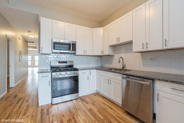 kitchen featuring sink, white cabinets, light wood-type flooring, tasteful backsplash, and appliances with stainless steel finishes