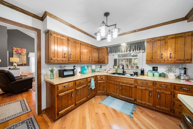 kitchen featuring hanging light fixtures, light wood-type flooring, sink, and crown molding