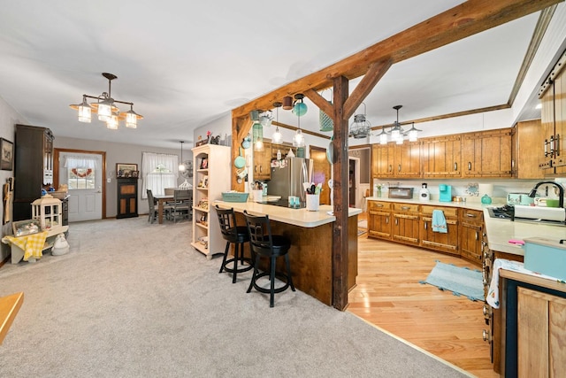 kitchen featuring kitchen peninsula, sink, hanging light fixtures, a breakfast bar area, and stainless steel fridge