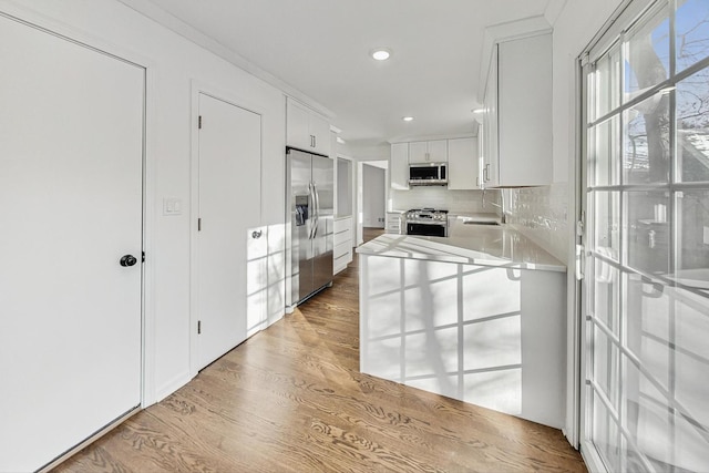 kitchen with stainless steel appliances, white cabinets, ornamental molding, light hardwood / wood-style floors, and decorative backsplash