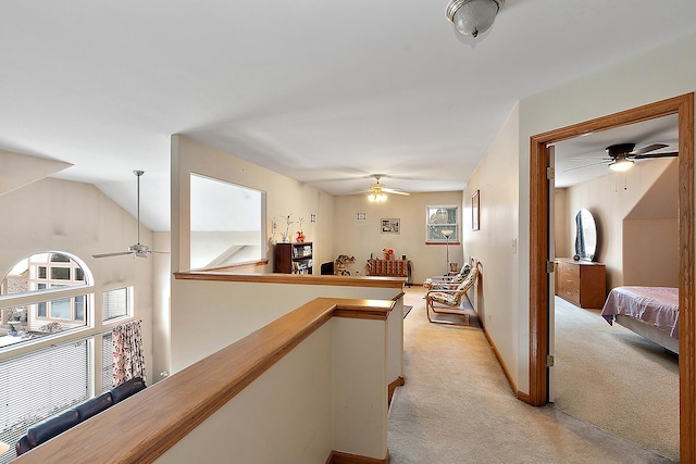 hallway featuring vaulted ceiling, a healthy amount of sunlight, and light colored carpet