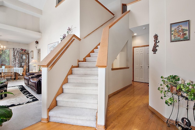 staircase featuring an inviting chandelier, a towering ceiling, and wood-type flooring