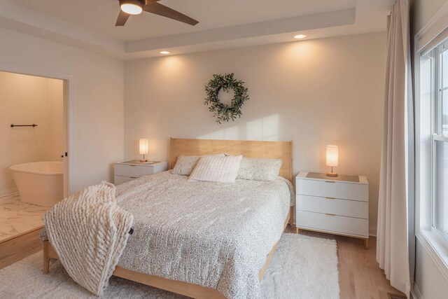 bedroom with light wood-type flooring, a raised ceiling, ceiling fan, and multiple windows