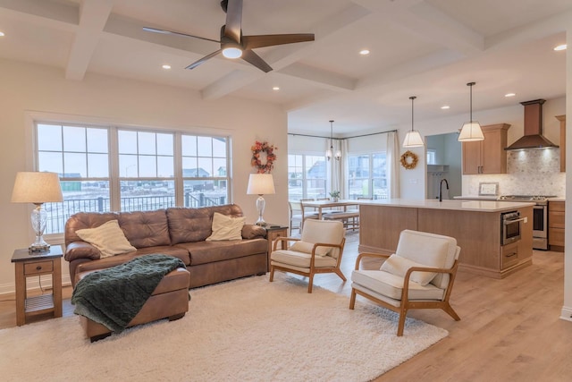 living room with sink, light wood-type flooring, ceiling fan with notable chandelier, coffered ceiling, and beam ceiling