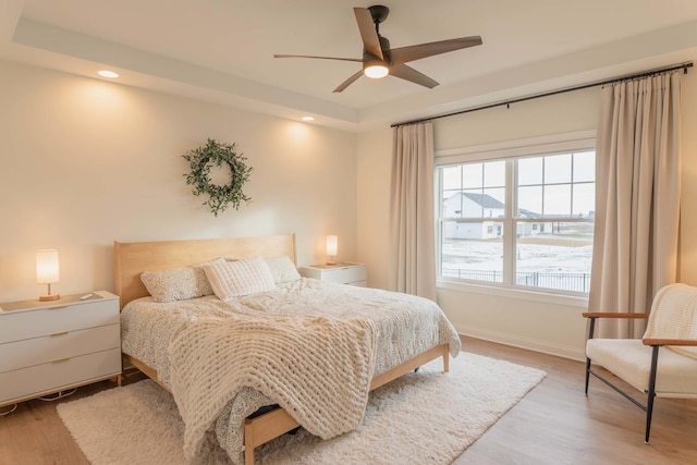 bedroom with ceiling fan, a tray ceiling, and light wood-type flooring