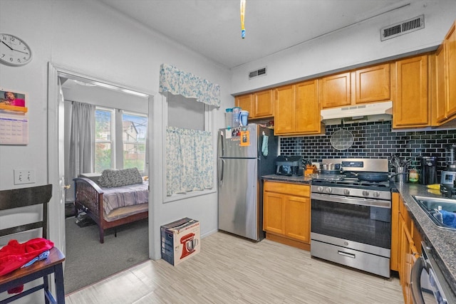 kitchen with stainless steel appliances, sink, light wood-type flooring, and tasteful backsplash