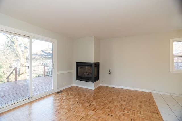 unfurnished living room with light parquet flooring, a multi sided fireplace, and a wealth of natural light