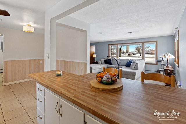 kitchen featuring light tile patterned floors, white cabinetry, wood walls, a baseboard radiator, and a textured ceiling