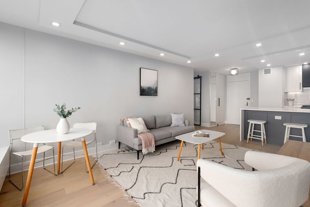 living room with light hardwood / wood-style floors and a tray ceiling