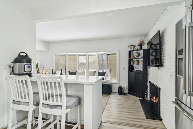 kitchen with light hardwood / wood-style flooring, a kitchen breakfast bar, high quality fridge, a brick fireplace, and kitchen peninsula