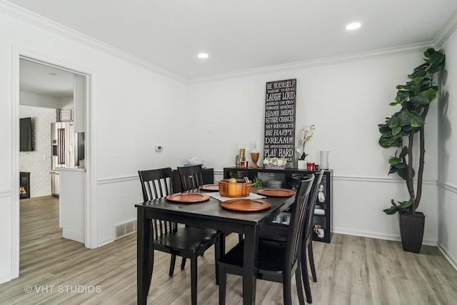 dining space with ornamental molding, a fireplace, and light hardwood / wood-style floors