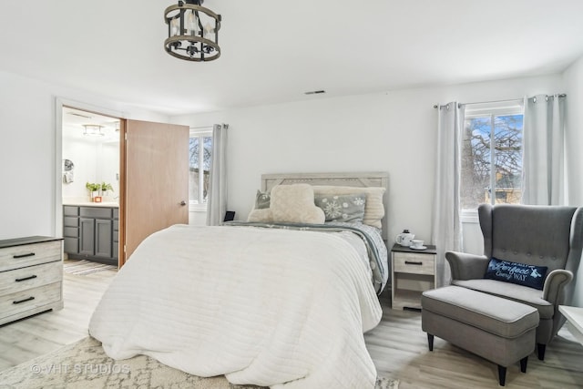 bedroom featuring light wood-type flooring, an inviting chandelier, and ensuite bath